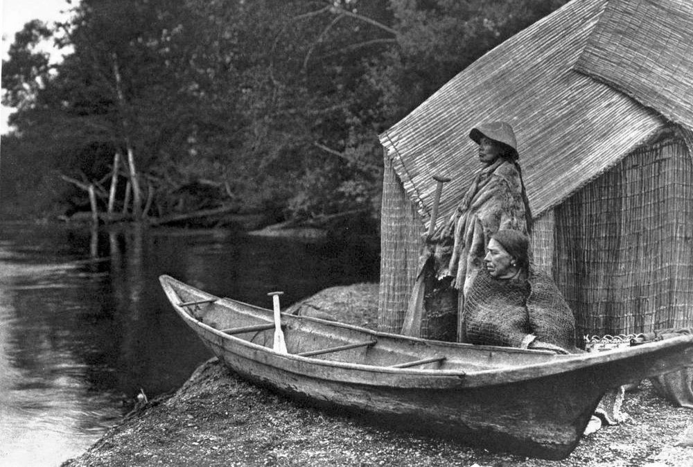 From “The North American Indian” by Edward S. Curtis; Volume 9; Plate No. 302; Skokomish fishing camp; two natives on beach, canoe in foreground.